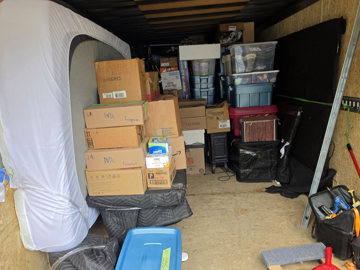 Labelled moving boxes, storage bins and a wrapped mattress loaded in a TCM Movers trailer