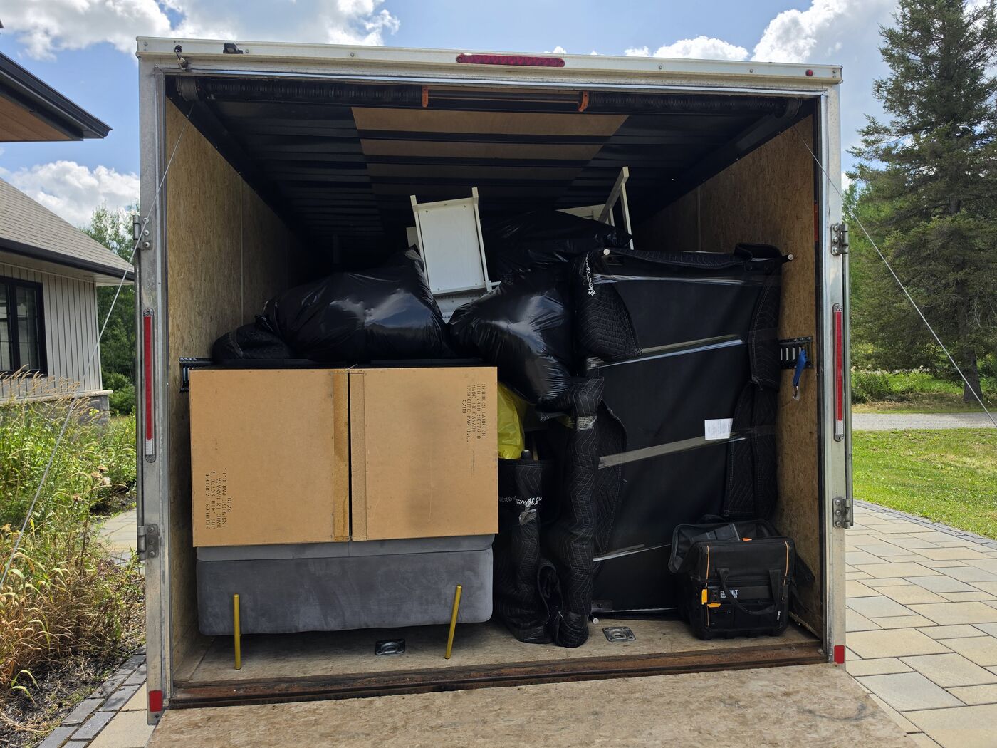 TCM Movers trailer loaded with wrapped furniture, parked in the driveway of a home